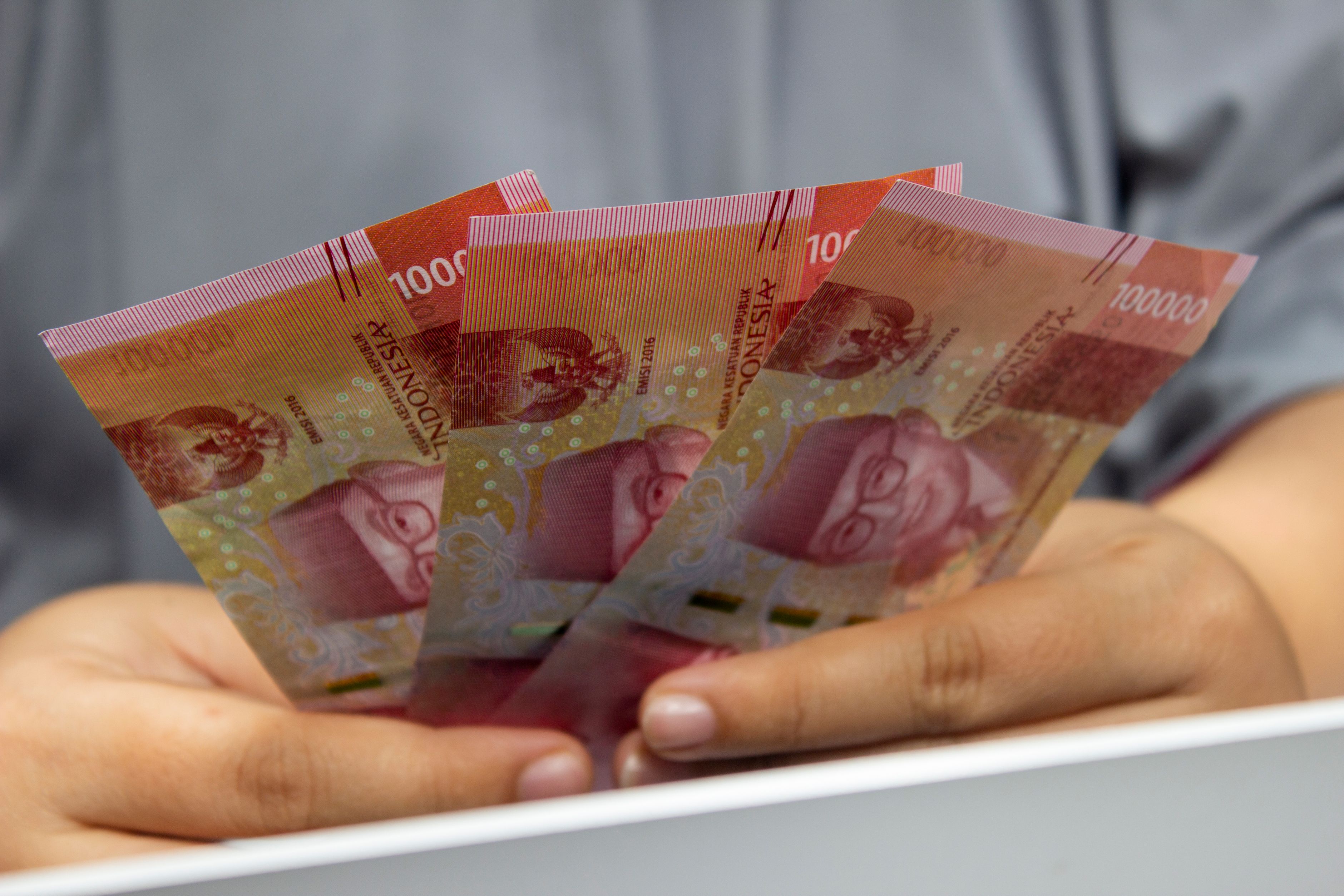 Tangan memegang lembaran uang kertas rupiah Indonesia, menggambarkan posisi kurs rupiah di kisaran Rp17.894 per dolar AS saat Bitcoin melonjak ke US$85.000 pada 1 Oktober 2026